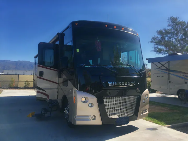 Front view of a sleek black and tan Winnebago motorhome RV rental, parked on concrete with mountains and another RV in the background.. Winnebago Vista 2016