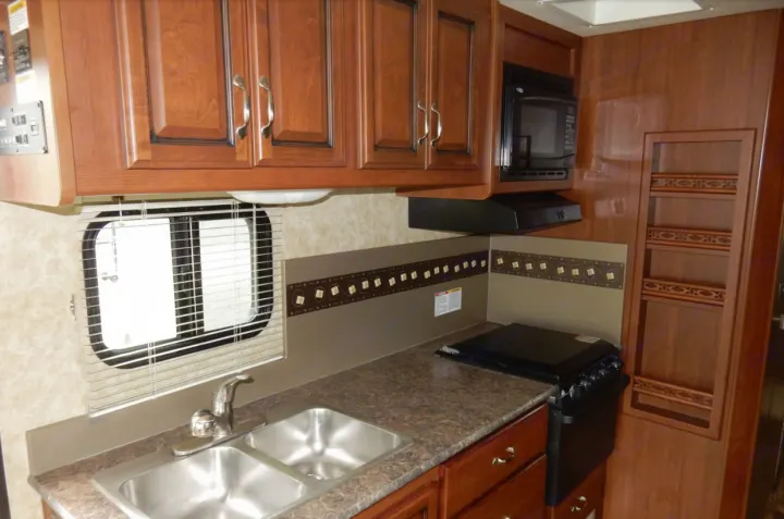Inside an RV rental: a compact kitchen with a double sink, stove, microwave, and wooden cabinets.. Fleetwood Storm 2013