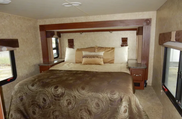 An inviting RV rental bedroom with a large bed, ornate headboard, and windows, offering comfortable sleeping arrangements for your travels.. Fleetwood Storm 2013