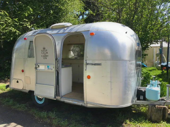 This classic silver Airstream RV rental is ready for adventure, door open revealing its cozy kitchen and a "Keep Calm" sign.. Airstream Caravel 1968