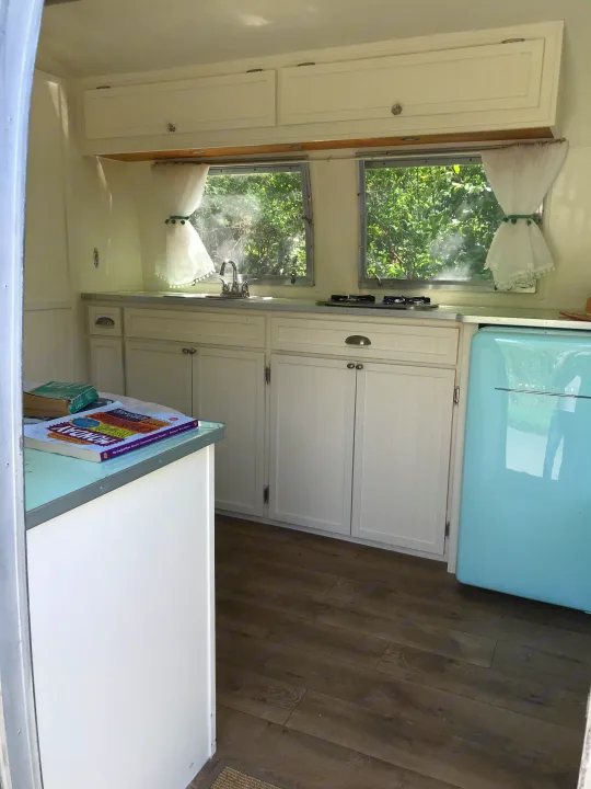 Bright RV rental kitchen featuring white cabinets, sink, stove, retro blue fridge, and scenic windows.. Airstream Caravel 1968