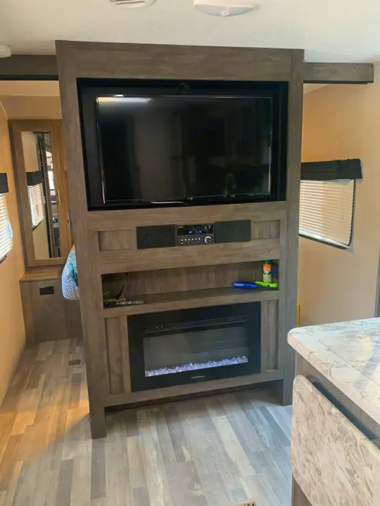 Modern RV rental interior featuring an entertainment center with a TV, stereo, and electric fireplace, complemented by sleek grey flooring.. Forest River Vibe 2021