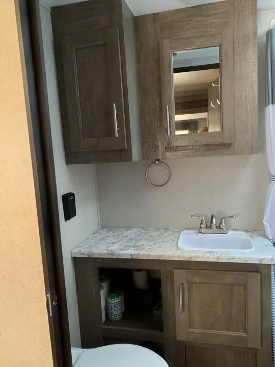 RV rental bathroom vanity with a white sink, mirror, upper and lower storage cabinets, offering compact functionality.. Forest River Vibe 2021