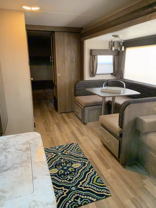 This bright RV rental interior features a U-shaped dinette, kitchen counter, and hallway to bunk beds. Modern style.. Forest River Vibe 2021