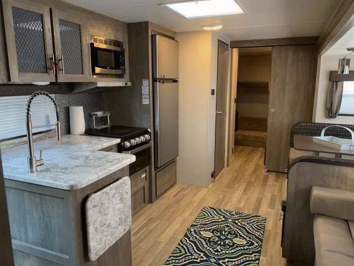 Modern RV rental interior with kitchen, dining booth, sofa, and bunk beds accessible via sliding door. Bright and inviting.. Forest River Vibe 2021