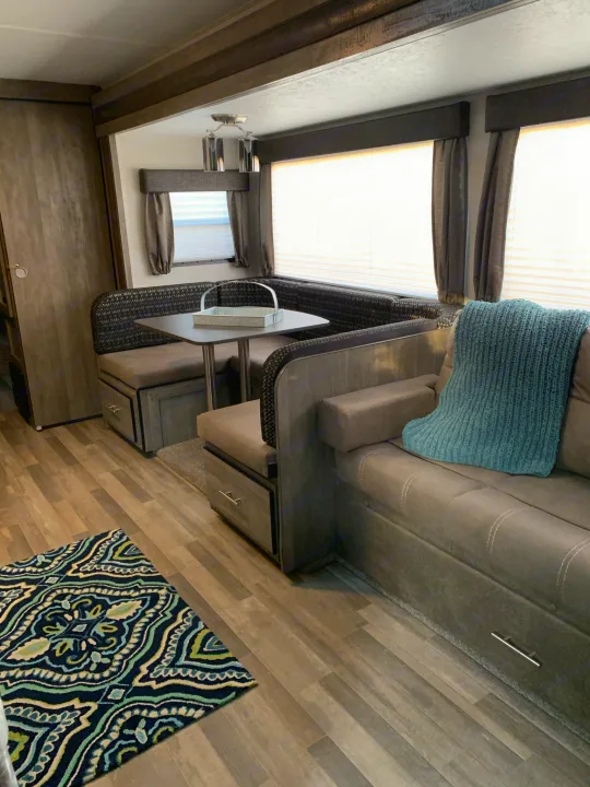 RV rental interior showcasing a comfortable U-shaped dinette, sofa with a blue blanket, and stylish wood-look flooring.. Forest River Vibe 2021