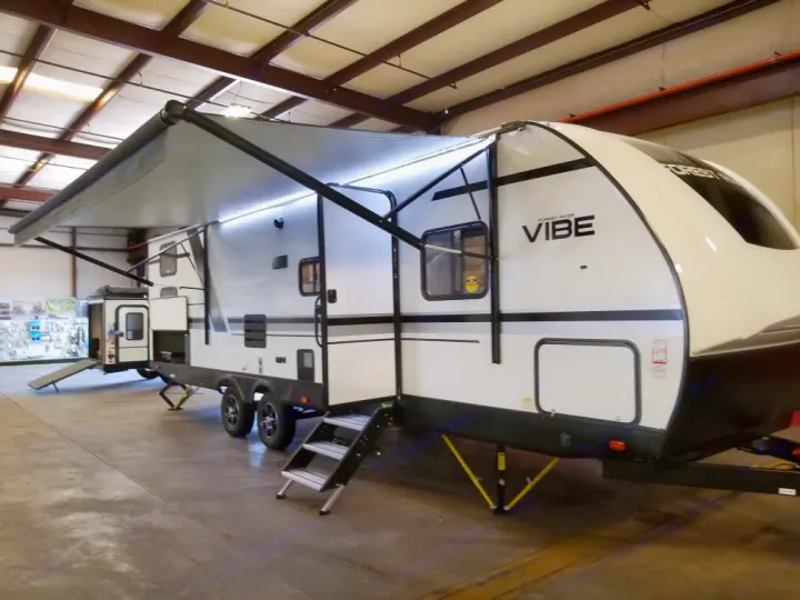 Bright white Forest River Vibe travel trailer with extended awning and steps in an RV showroom, ready for your RV rental.. Forest River Vibe 2021