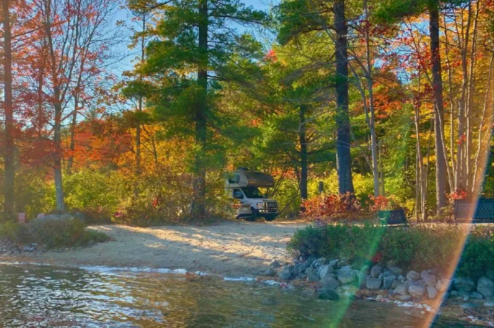 Discover fall beauty with an RV rental! Camper van parked by a serene lakeside path, surrounded by vibrant autumn trees.. Thor Quantum 2017