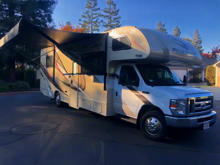 White Thor Four Winds Class C RV rental with extended awning parked on asphalt.. Thor Four Winds 2020