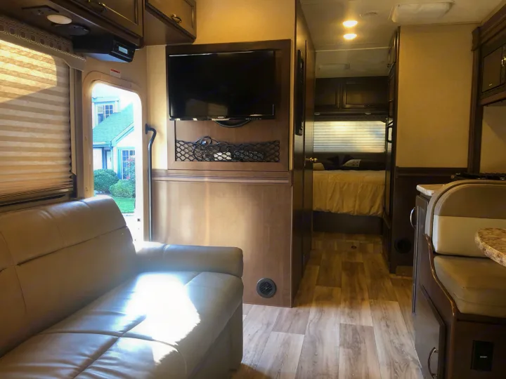 Inside a spacious RV rental: a living area with a sofa and TV, a dining booth, and a view into the bedroom.. Thor Four Winds 2020