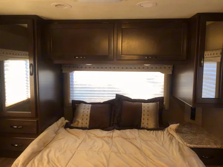 Cozy RV rental bedroom featuring a bed, overhead cabinets, and side storage with mirrors, perfect for travel.. Thor Four Winds 2020