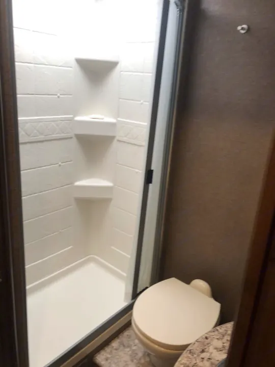 Inside this RV rental, find a clean, compact bathroom featuring a white shower stall with shelving and a toilet.. Thor Four Winds 2020