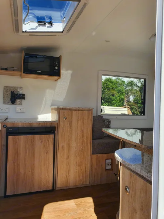 Inside a bright RV rental: compact kitchen with microwave/fridge, speckled counters, cozy dining booth.. Avan Aspire 402 2018