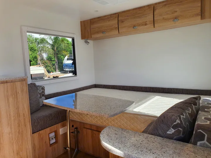 Bright RV rental interior with convertible bed/dinette, wood storage, and large window overlooking nature.. Avan Aspire 402 2018