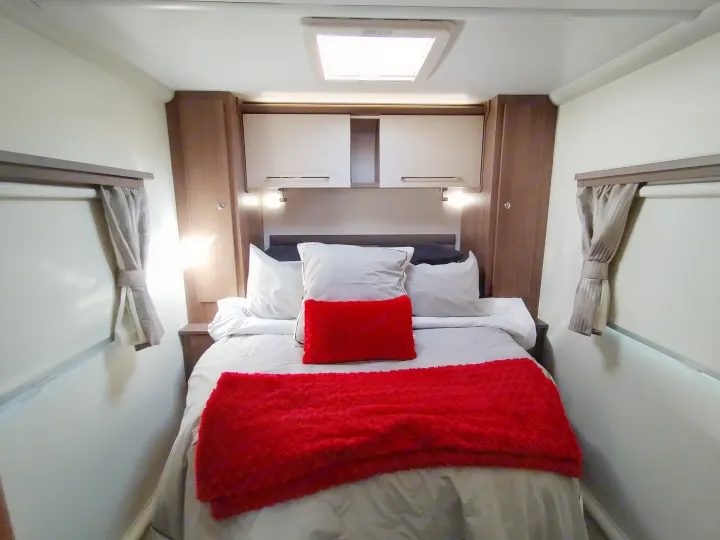 Cozy RV rental bedroom with a queen bed, bright red accents, built-in cabinets, and soft ambient lighting for comfort.. Bailey Pheonix 640 2022
