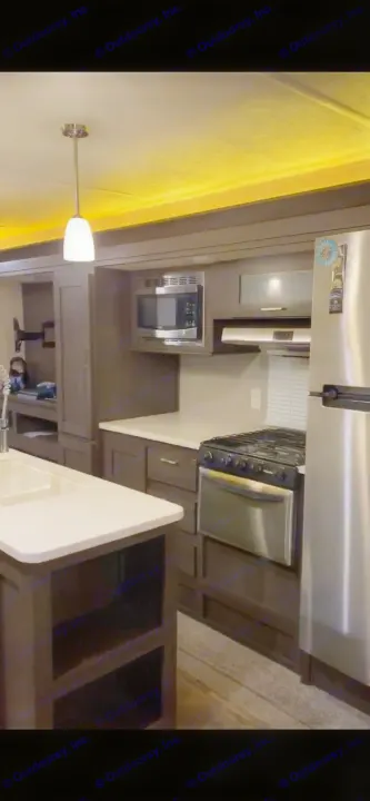 Modern RV rental kitchen featuring dark cabinets, white countertops, stainless steel appliances, and a central island with sink.. Forest River Wildwood 2018