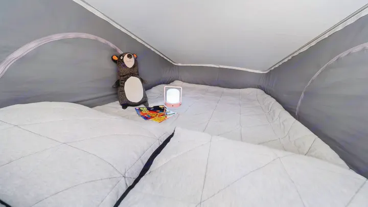 Comfortable pop-top sleeping area inside an RV rental, with quilted bedding, a plush bear, and a glowing lamp.. Winnebago Winnebago 2021