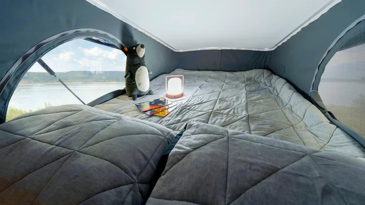 Cozy RV rental pop-top bed with quilted gray bedding, bear, and glowing lamp, offering a scenic lake view for peaceful nights.. Winnebago Winnebago 2021