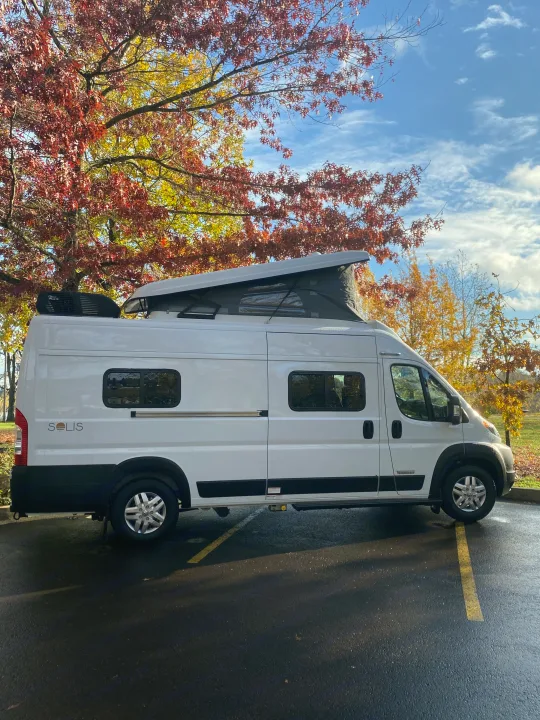 White Winnebago Solis RV rental with pop-top, parked under bright autumn foliage. Ready for your road trip!. Winnebago Winnebago 2021