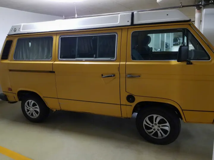 Yellow vintage VW camper van with pop-top roof. Ideal RV rental for adventures, parked in a concrete garage.. Volkswagen Westfalia 1982