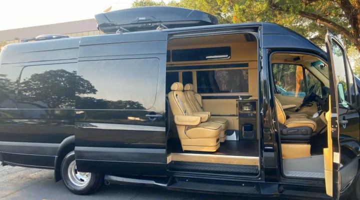 Luxury black RV rental with open doors showing a plush beige interior and custom captain's chairs, ideal for travel.. Mercedes-Benz Sprinter 2015
