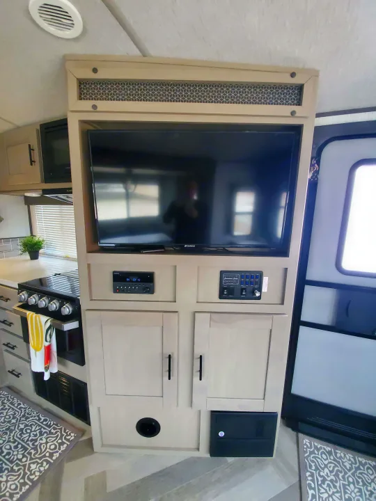 RV rental interior: a media wall with TV, control panels, and light wood cabinets. Below, a kitchen with stove and microwave.. Cruiser Rv Corp Cruiser 2021