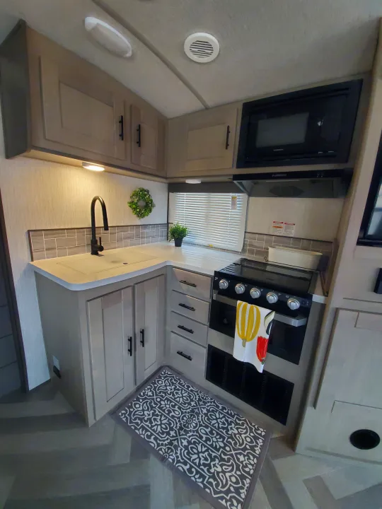 Inside this RV rental, a compact kitchen features a light-colored countertop, sink, black stove, microwave, and multiple cabinets.. Cruiser Rv Corp Cruiser 2021