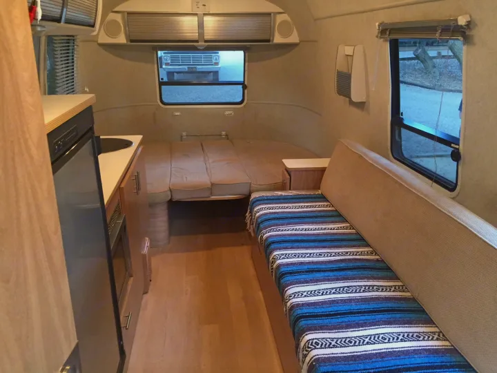 Compact RV rental interior featuring a kitchen, convertible bed, and cozy bench seating with a vibrant blanket.. Airstream Safari 2008