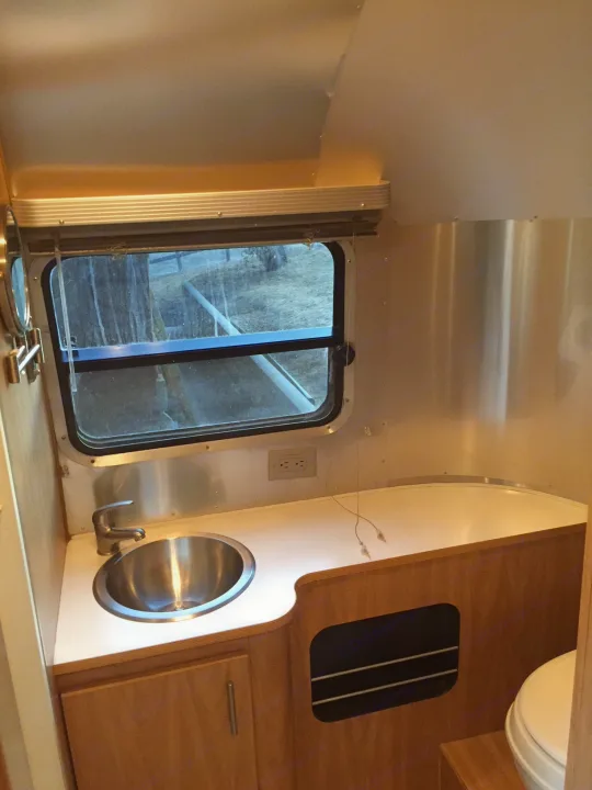 RV rental interior: shiny aluminum walls, a compact kitchen with sink and wooden cabinets, plus a window view.. Airstream Safari 2008