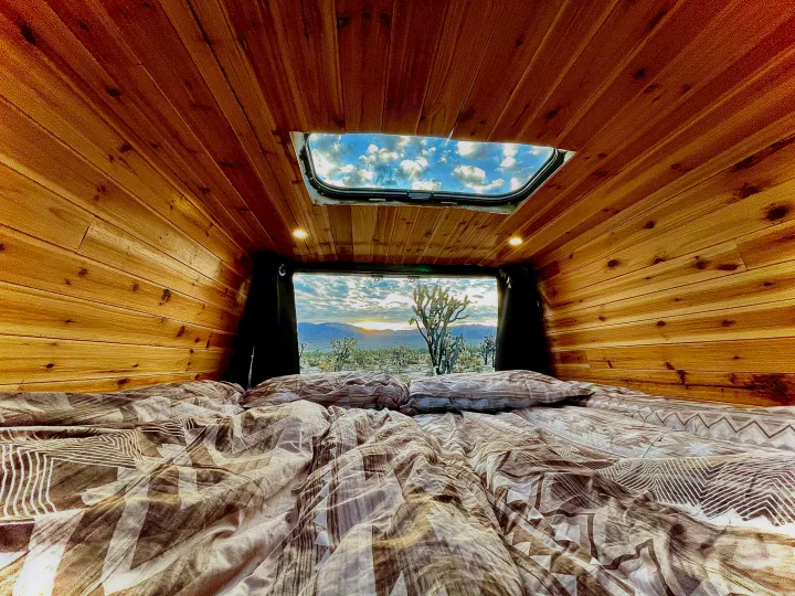 Cozy RV rental interior with bed and wood paneling, offering stunning desert sunset views and a sky through the roof.. Mercedes-benz 4x4 Sprinter mwb 2019
