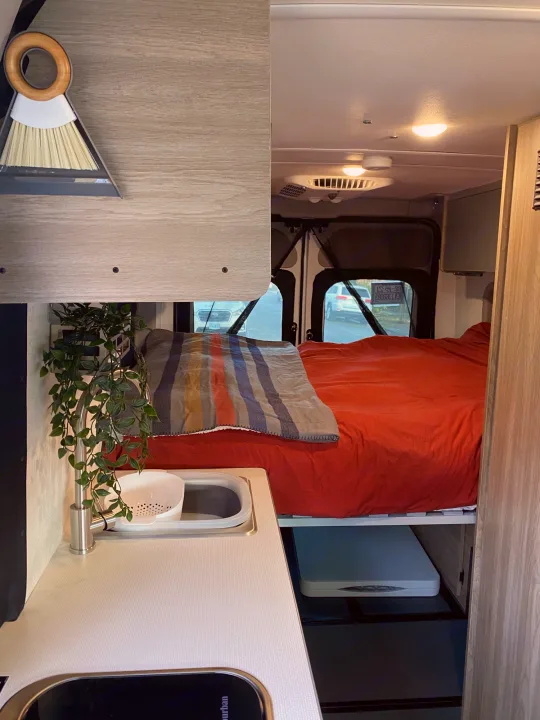Inside a functional RV rental: comfy bed, compact kitchen with sink, and hanging plant. Includes a broom and dustpan.. Winnebago Winnebago 2021