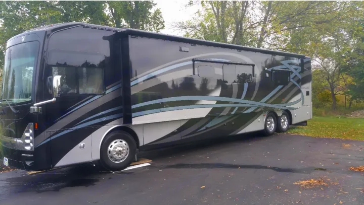 Spacious black and silver Tuscany RV rental, a luxurious Class A motorhome parked outdoors amidst trees.. Thor Motor Coach Tuscany 2016