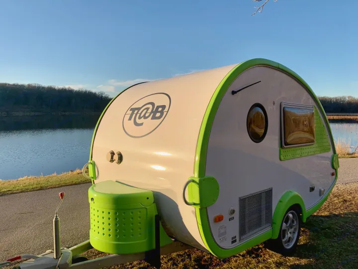 This bright T@B teardrop RV rental, lime green and white, sits by a sunny lake, ready for adventure.. T@B T16 2008
