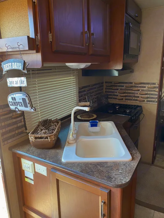 This RV rental kitchen features a sink, stove, microwave, and wooden cabinets, ideal for comfortable travels on the road.. Jayco Redhawk 2014