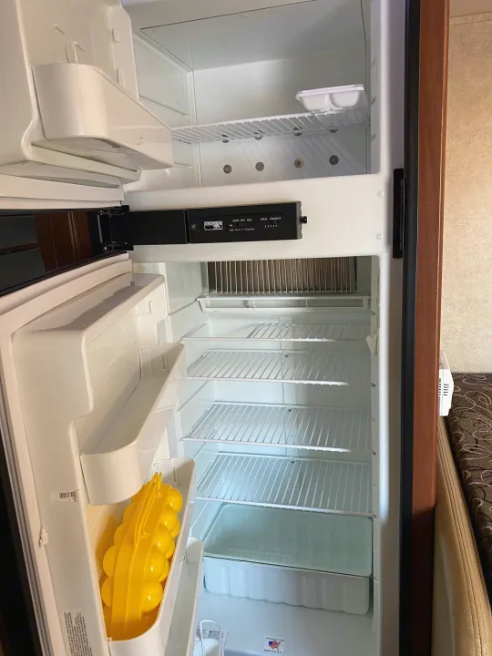 Clean, empty RV rental refrigerator, ready for your food. Features interior shelves, door storage, and a yellow ice mold.. Jayco Redhawk 2014