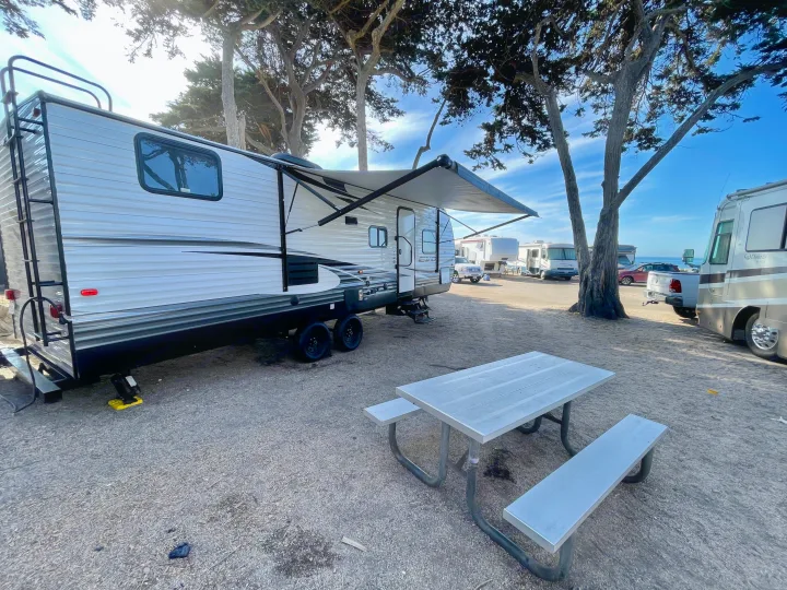 RV rental travel trailer parked at a treed campsite with a picnic table, hinting at a coastal view.. Forest River Evo T2550 2019