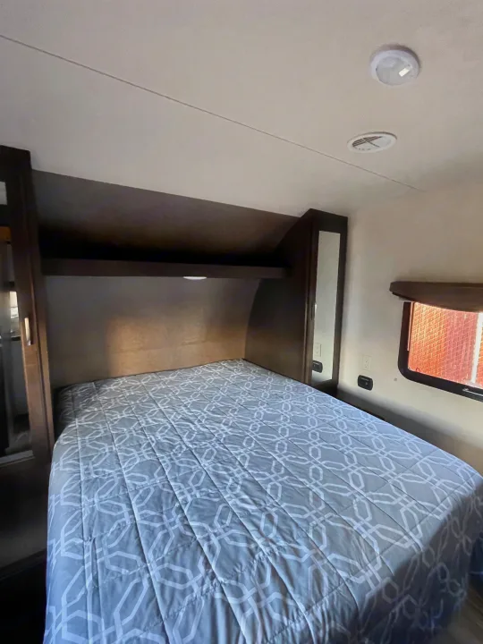 Comfortable RV rental bedroom with a grey patterned bed, built-in storage, and ceiling vents.. Forest River Evo T2550 2019