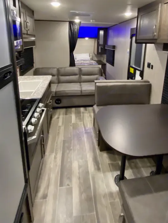Bright rv rental interior featuring a kitchen, sofa, dinette, and a curtained bedroom. Wood-look flooring completes the modern feel.. Jayco Jay Flight SLX 2021
