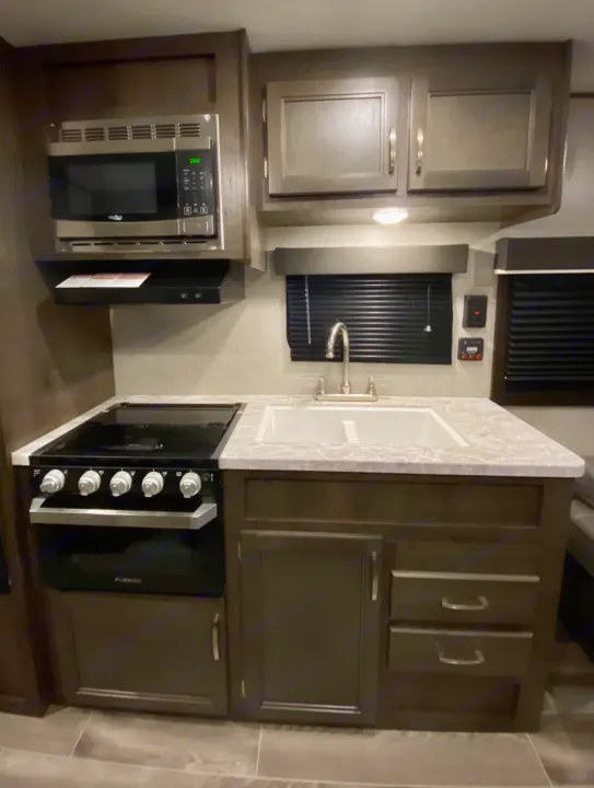Well-equipped RV rental kitchen featuring a microwave, stove, sink, and dark cabinets. Ready for your adventures.. Jayco Jay Flight SLX 2021