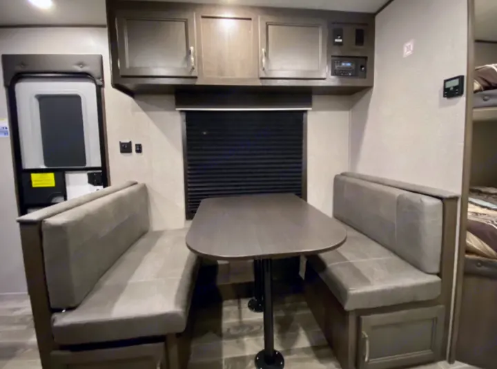 This RV rental dinette has comfy gray benches & table, overhead cabinets, and bunk beds visible for cozy travel.. Jayco Jay Flight SLX 2021
