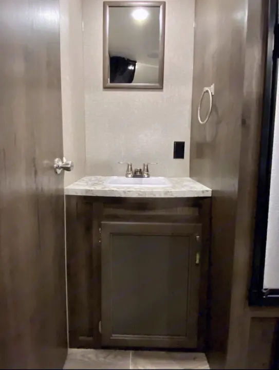 RV rental bathroom featuring a wooden vanity, white sink, chrome faucet, mirror, and dark cabinet. A functional space.. Jayco Jay Flight SLX 2021