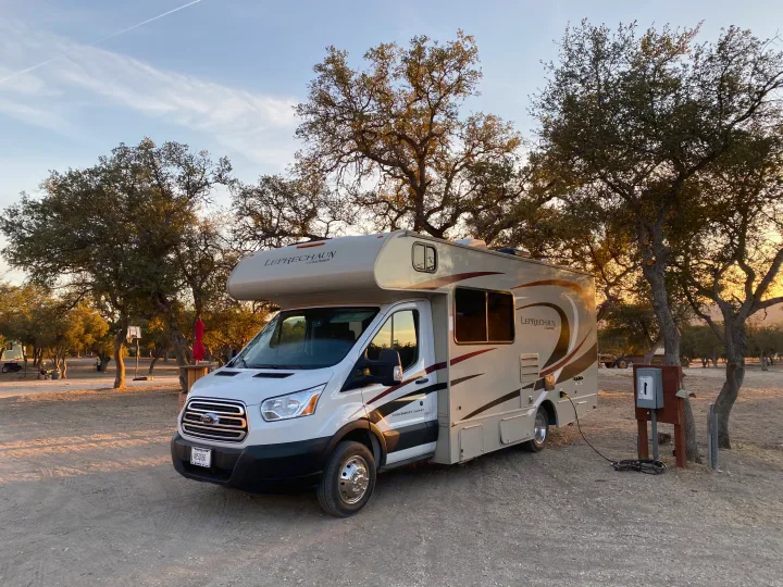 RV rental parked at a serene campsite with trees, plugged into power. The Class C motorhome enjoys the golden hour.. Other Other 2020