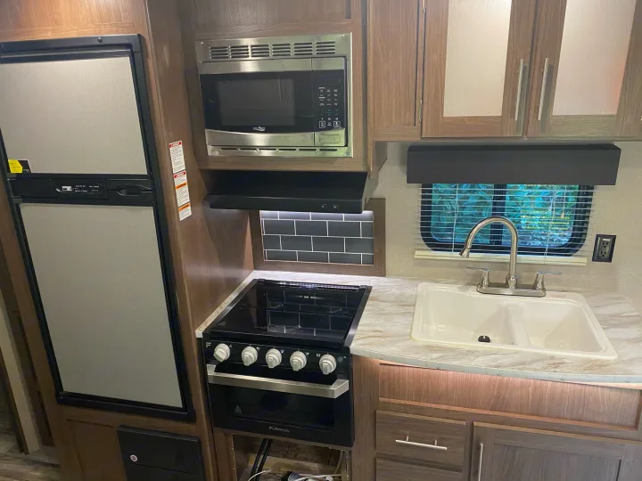 Three burner gas stove/gas oven. ventilation hood with light, microwave oven overhead. Refrigerator and freezer can run off of electricity or propane. Double bowl sink with storage below and above.. Keystone Hideout 2020