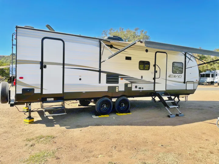 Spacious RV rental travel trailer with awning deployed at a sunny campsite under clear blue sky, ideal for trips.. Forest River Evo 2850 2019