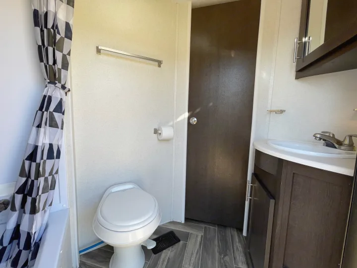 RV rental bathroom: shower with geometric curtain, toilet, sink vanity, and wood-look tiled floor.. Forest River Evo 2850 2019