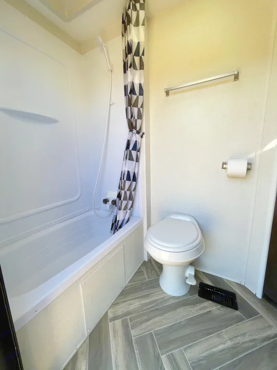 RV rental bathroom showcasing a clean tub/shower combo with patterned curtain, toilet, and towel bar. Compact & functional.. Forest River Evo 2850 2019