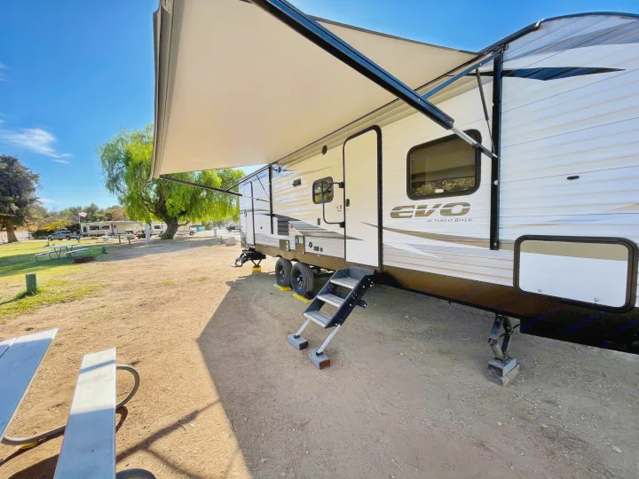RV rental set up at a sunny campground with awning, steps, and picnic table. Ready for camping adventures.. Forest River Evo 2850 2019