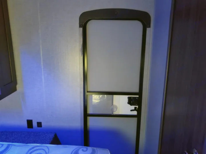 Cozy RV rental interior featuring a white door, blue-lit wall, power outlets, and a comfortable bed setup.. Crossroads Zinger 2018
