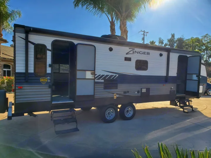 This Zinger travel trailer, a spacious RV rental, is parked with open doors and extended steps on a sunny day.. Crossroads Zinger 2018
