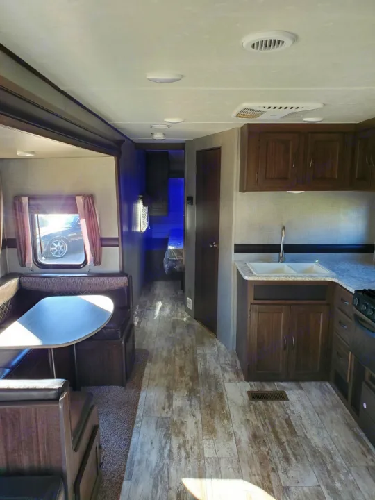Inside this modern RV rental: a kitchen, dining booth with wood-look flooring, and hallway leading to a bedroom.. Crossroads Zinger 2018